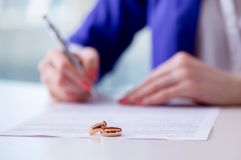 A person filling out a form with two wedding rings sitting on top of the form.